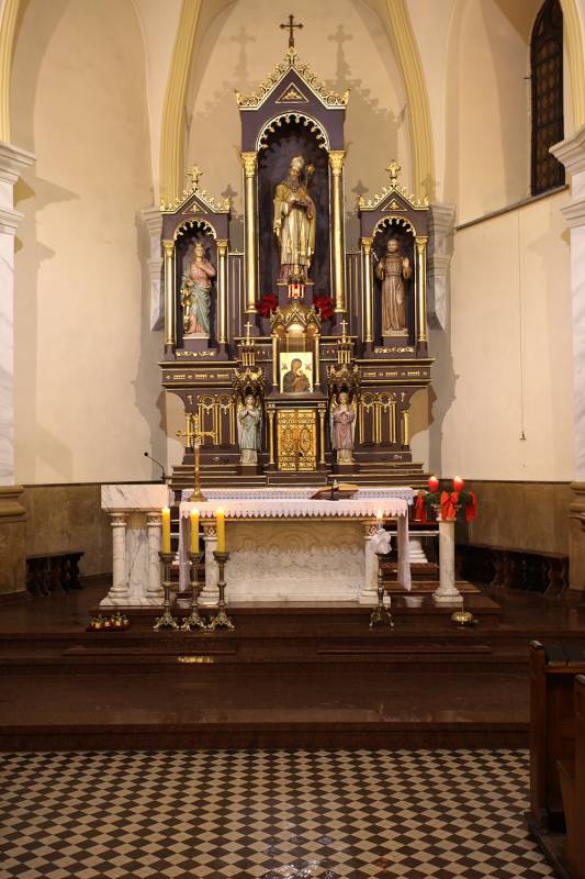 Kościół p.w. Św. Mikołaja nr 2 (Wnętrze Kościoła. Ołtarz główny w kolorze białym z zdobieniami. Przed nim trzy świeczniki ze świecami. W tle tabernakulum, obraz Matki Bożej oraz trzy figury.)