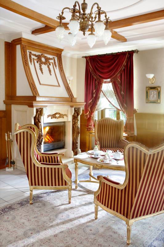 Pałac w Czarnym Lesie nr 5 (Sala z kominkiem, w środku stolik kawowy z trzema dużymi fotelami w kolorze złotym i czerwonymi pasami.)