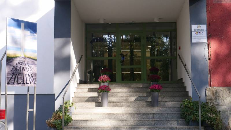 Oblackie Centrum Młodzieży NINIWA nr 2 (Wejście do Oblackiego Centrum Młodzieży NINIWA. Szare schody, z doniczkami z różowymi kwiatami, prowadzące do wejścia. Zielone przeszklone drzwi. Przed wejściem tablica z napisem: Jezus jest drogą, prawdą, życiem.)
