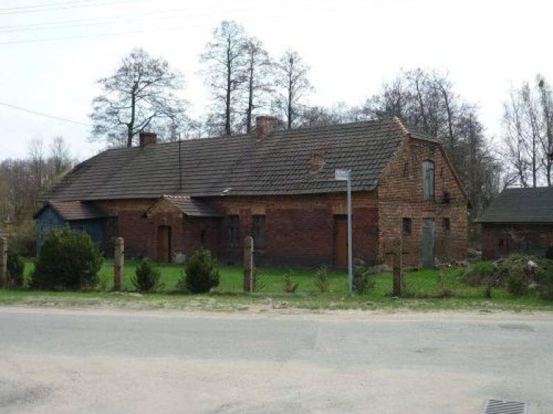 Karczma nr 1 (Frontowa część budynku Karczmy. Budynek w kolorze cegieł otoczony trawnikiem oraz płotem.)