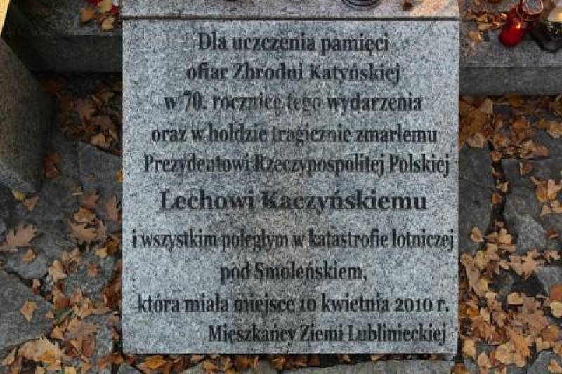 Tablica na Cmentarzu Wojskowym nr 1 (Szara tablica, na niej napis w kolorze czarnym. W tle brązowe liście i ciemnoszare podłoże.)