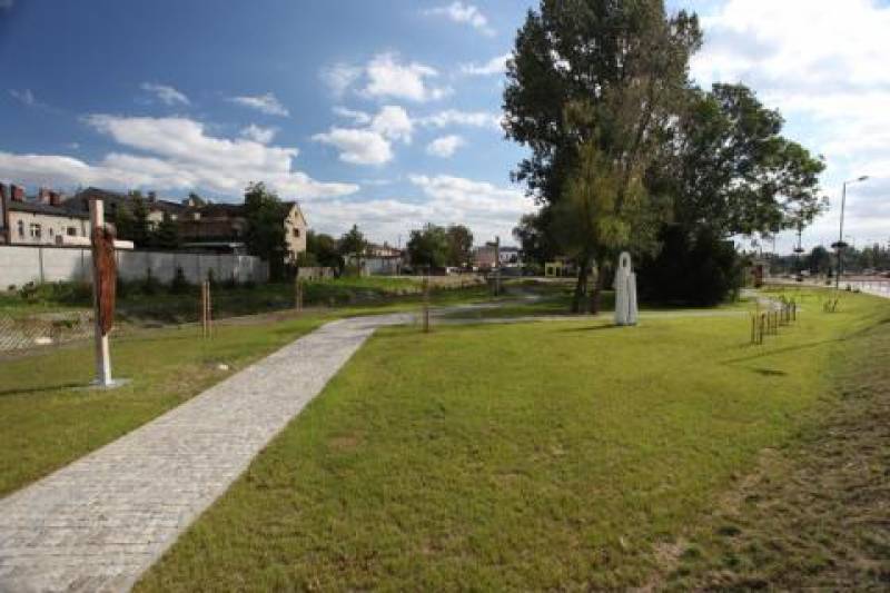 Skwer im. Rodziny Stein nr 1 (Skwer im. Rodziny Stein. Chodnik otoczony trawą. W tle rzeźby, drzewa oraz budynki.)