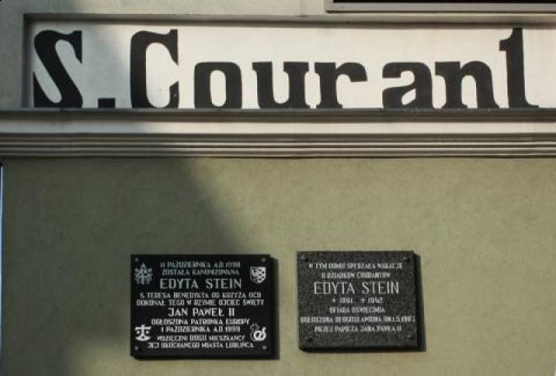 Tablica na kamienicy, w której mieszkali dziadkowie św. Edyty Stein nr 1 (Dwie czarne tablice na zielonym tle. Napisy w kolorze białym. Nad tablicami, na białym tle, czarny napis: S. Courant.)