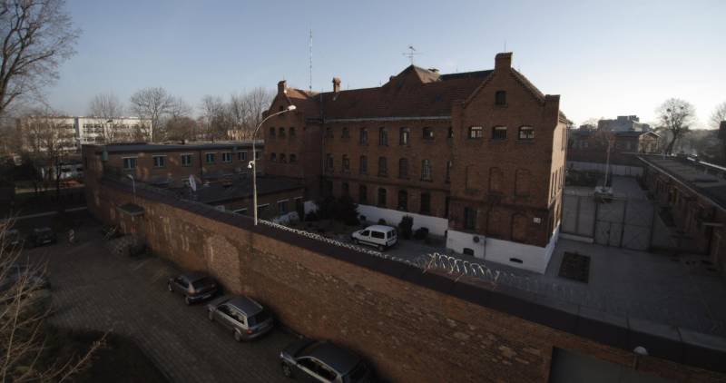 Zespół więzienia (Ceglany budynek więzienia otoczony murem. Wewnątrz widoczny biały samochód. Na zewnątrz ustawione w rzędzie samochody.)