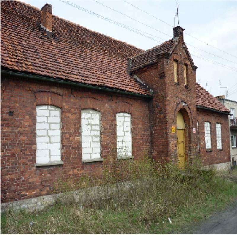 Zespół Budynków Szkolnych w Boronowie nr 1 (Frontowa część tzw. Niskiej Szkoły. Budynek w kolorze cegieł. Okna zamurowane białym materiałem budowlanym.)