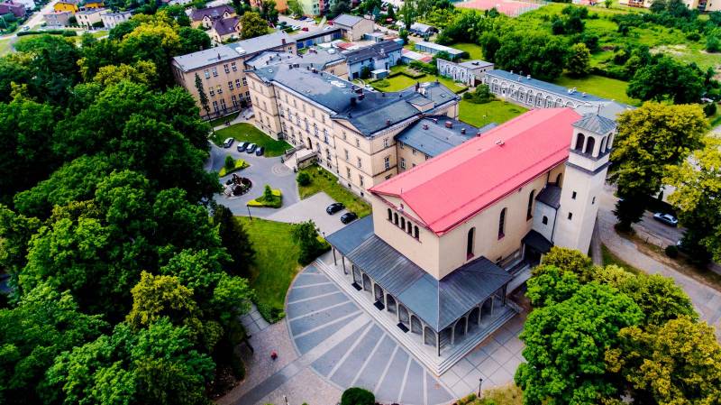 Parafia św. Stanisława Kostki w Lublińcu nr 1 (Widok z lotu ptaka, budynek parafii posiada czerwony dach, na wejściu do parafii szerokie schody na których podparty jest daszek betonowymi filarami, widoczny cały kompleks klasztoru i parafii)